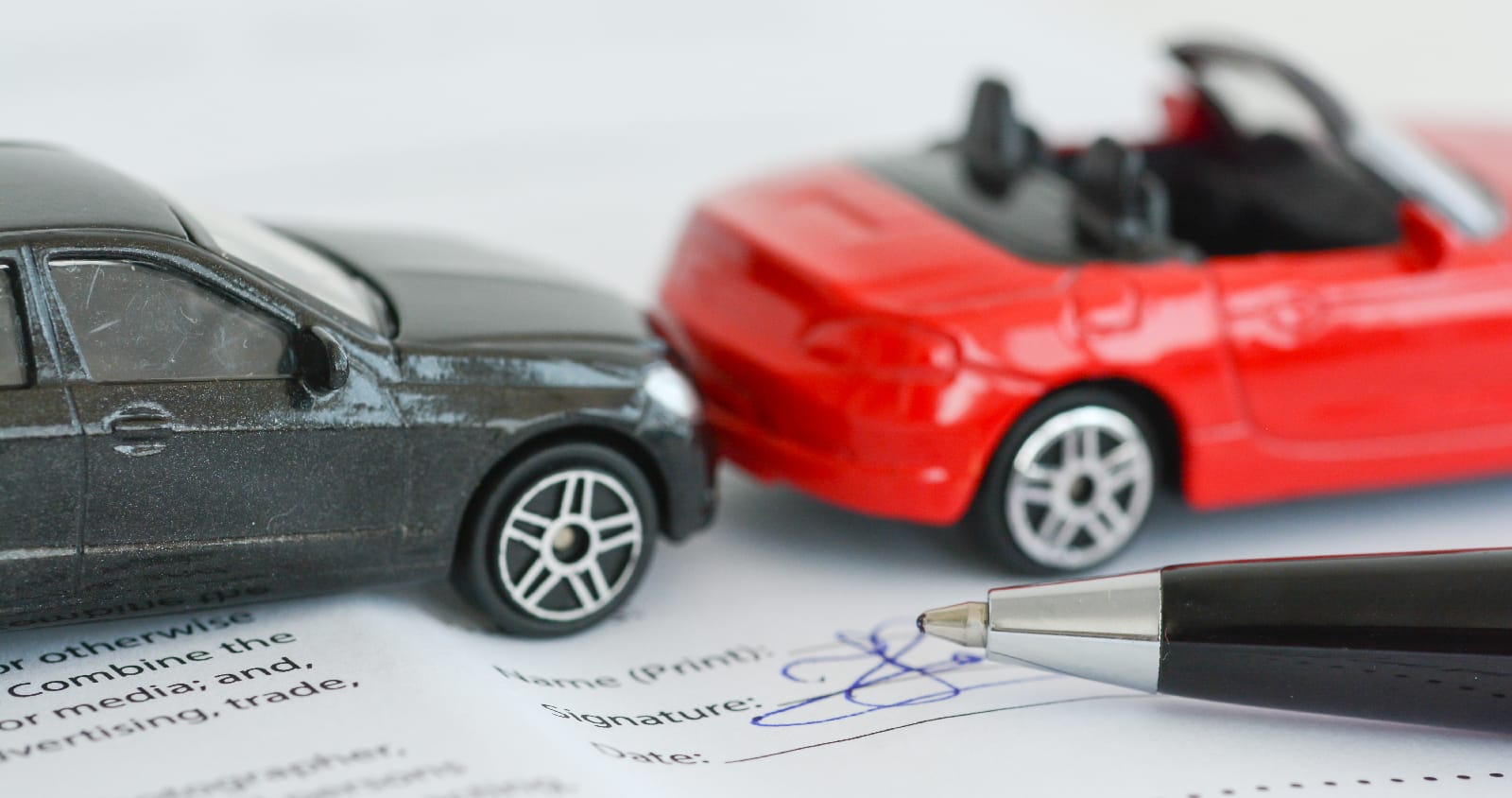 toy cars in a fender bender with a car insurance document below